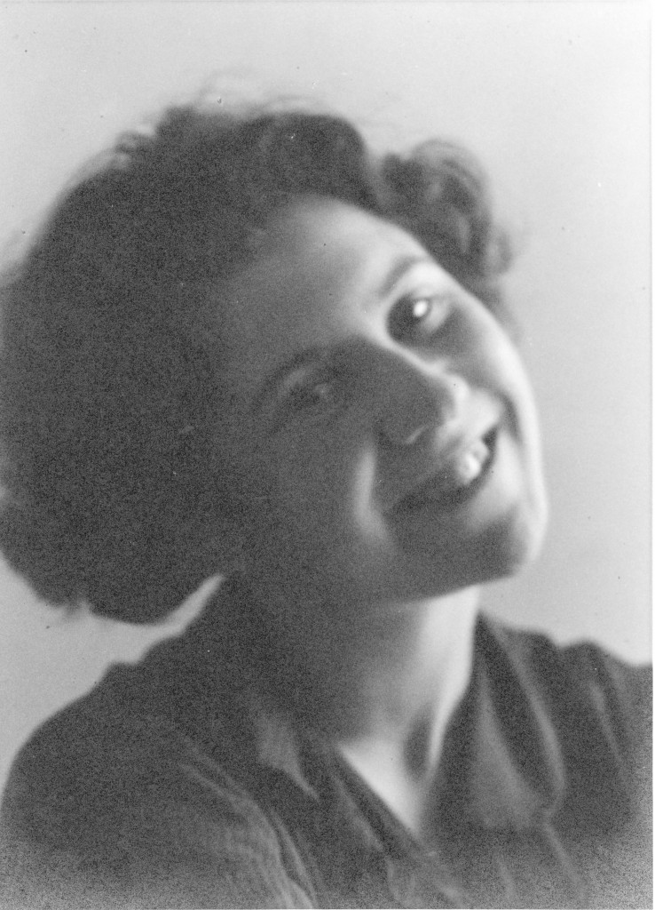 Een zwart/wit portret van Etty Hilesum. Ze kijkt met een gekanteld hoofd lachend de camera in.